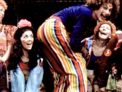 Performers in colorful costumes laugh and pose together onstage during a 1972 Toronto production of “Godspell.”