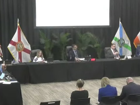 Coral Gables city commissioners sit behind a long black-draped table during an inspector general workshop, with several attendees seated in the foreground and flags behind the dais.