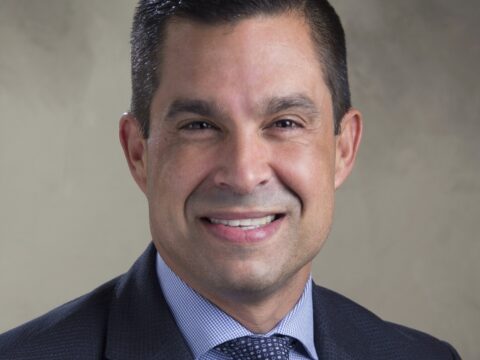 Head-and-shoulders portrait of Coral Gables Mayor Vince Lago smiling in a dark suit, blue checked shirt and patterned tie against a neutral background.