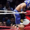 Two masked little-person Lucha Libre wrestlers compete in a wrestling ring as spectators watch from the background.