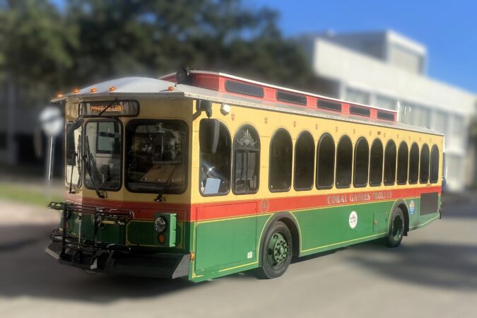 Cream, red and green Coral Gables trolley displaying the Ponce de Leon route against a softly blurred city background.